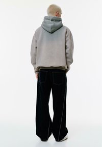 Overdimensioneret grå gradient hoodie med hætte, parret med sorte vide jeans med kontrasterende hvid syning og baglommer.