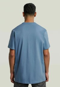 Niebieska bawełniana koszulka z krótkim rękawem, okrągłym dekoltem i luźnym krojem. Gładka faktura, jednolity kolor, bez widocznych wzorów ani akcentów.