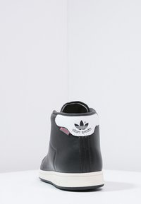 Svart läder hög sneakers med vit ankelkrage, präglad logotyp och minimalistisk design. Gummisula med tonala accenter.