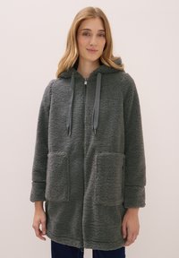 Chaqueta de forro polar gris y esponjosa con cremallera en la parte delantera, capucha y dos bolsillos frontales. Presenta cordones ajustables y una textura suave.