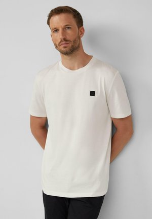 White short-sleeve t-shirt in a soft fabric, featuring a small black logo patch on the left chest, crew neckline, and relaxed fit.
