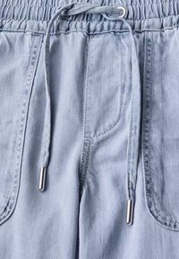 Pantalones de chándal de algodón azul claro con cinturilla elástica y cordón. Cuenta con dos bolsillos laterales y tela texturizada. Detalles metálicos en color plata.