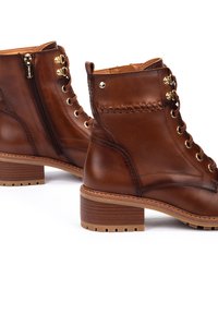 Bottines en cuir marron avec des accessoires en métal doré, lacées sur le devant, avec une fermeture éclair sur le côté et des détails de couture texturée. Talon carré et semelle en caoutchouc.