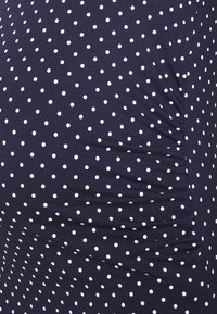 Tummansininen kangas, jossa on valkoisia pilkkuja, hieman poimuttunut oikealta puolelta, mikä näyttää materiaalin tekstuurin ja venyvyyden.