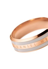 Sormus ruusukultaisesta metallista, jossa on valkoiset emaliraidat ja kaiverrettu "DANIEL WELLINGTON" -yksityiskohta. Sileä pinta; tyylikäs, pyöristetty muoto.