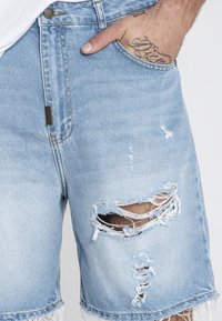 Svijetloplave traper šorts hlače s istrošenim dizajnom, griffinim rubovima, velikim rupama i klasičnim pet džepnim stilom.