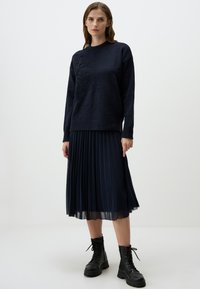 Maglione a maglia blu scuro con un design floreale testurizzato, abbinato a una gonna plissettata blu scuro e stivali da combattimento in pelle nera.