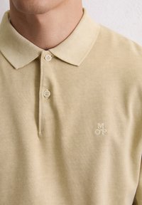 Beżowa bawełniana koszulka polo z klasycznym kołnierzykiem, trzema guzikami i wyszywanym logo "MOP". Miękka faktura i minimalistyczny design.