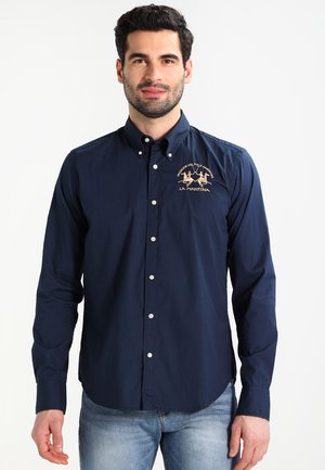 Camicetta lunga in cotone blu navy con chiusura a bottoni, dotata di un logo ricamato sul lato sinistro del petto e design del colletto classico.