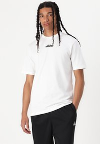 Hvit bomulls t-skjorte med korte ermer og svart Adidas-logo på brystet, kombinert med svarte treningsbukser med liten Adidas-emblem.