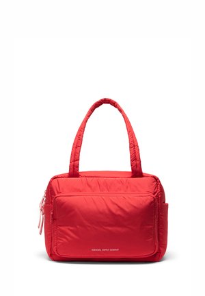 Jasne červená polstrovaná taška typu tote s dvoma rúčkami, veľkým predným vreckom na zips a bočným vreckom. Na prednej strane biely text „"Herschel Supply Company"“.