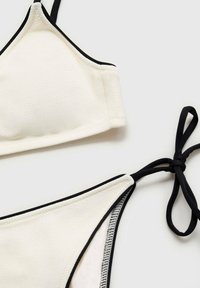 White bikini top and bottoms with black trim; top features thin straps and soft texture. Bottoms have side tie detail and contrasting lining.