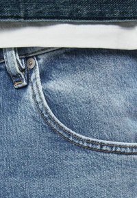 Blå denimjeans med en krökt ficka med brassnitsdetalj, blekta områden och kontrasterande sömmar längs sömmarna.