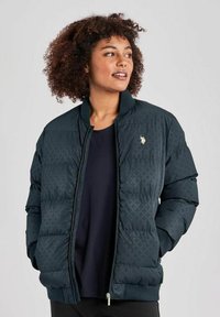 Zateplená bomber bunda v tmavozelenej farbe, s jemným vzorom, rebrovaným golierom a malým logom na hrudníku. Zapínanie na zips a bočné vrecká.