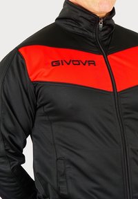 Zwarte en rode ritsjack met hoge kraag; heeft het logo "GIVOVA" in het zwart op de linkerborst. Glad textuur.
