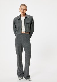 Chaqueta gris corta con dos bolsillos frontales, combinada con pantalones acampanados grises. El modelo lleva una camiseta blanca y zapatos de punta metálica.