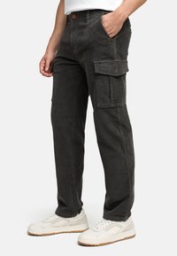 Mørkegrå corduroy cargo bukser med en tekstureret overflade, der har flere lommer og en knaplukning, parret med hvide sneakers.