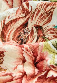 Textiel met bloemendessins in tinten van rood, roze, crème en groen, met een gestructureerde afwerking en verhoogde details op een zachte stof.