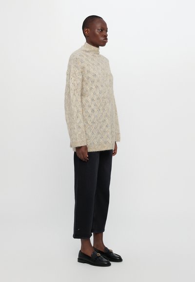 Lichtbruine gebreide trui met een hoge hals, voorzien van een textuur met ruitpatroon. Gecombineerd met donkere, cropped jeans en zwarte instappers.