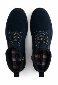 Une paire de bottes lacées en daim bleu marine avec une doublure intérieure à carreaux et une fermeture éclair sur le côté, vue de dessus sur un fond blanc.