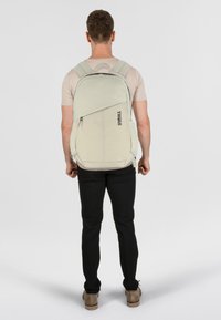 Sac à dos Thule gris clair avec des sangles ergonomiques, des compartiments zippés et un détail de logo. Forme rectangulaire, tissu durable et design élégant.