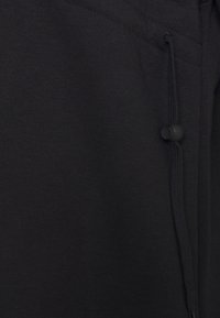 Pantalon de survêtement noir en mélange de coton avec une texture lisse, doté d'une taille ajustable et d'un cordon de serrage avec un bouton rond.