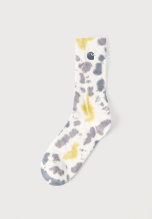 Hvid sok med grå og gule tie-dye mønstre, med et lille broderet øje nær den øverste kant.