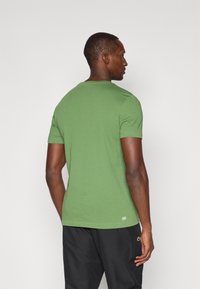 Zaļa īs�ām piedurknēm t-krekls no mīksta auduma, ar apaļu kaklu un šauru piegriezumu, ar mazu logotipu apakšējā muguras daļā.