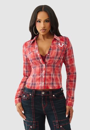 Czerwona koszula w kratę na guziki z długimi rękawami i dopasowanym krojem. Z białymi akcentami i kołnierzykiem, zestawiona z ciemnymi dżinsami z czerwonym przeszyciem.