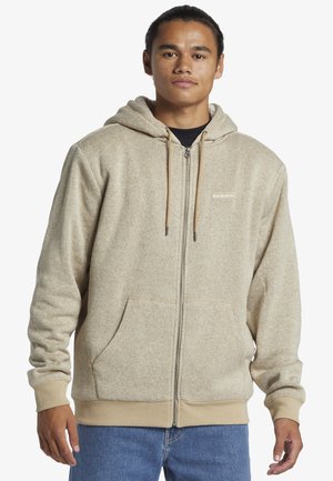 Beige zip-up hoodie with a hood, front pockets, and ribbed cuffs. Features a textured fabric and a small logo on the chest.