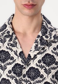 Κοντομάνικο πουκάμισο σε κρέμ ύφασμα, με ναυτικό λουλούδι σχεδίου που περιλαμβάνει τριαντάφυλλα και φύλλα, και κλασικό σχέδιο γιακά.