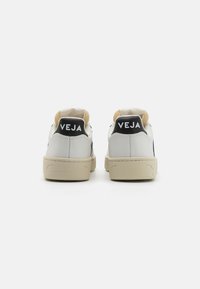 Hvite lær sneakers med beige detaljer, med en svart logo på hælen og en teksturert gummisåle. Rent design, low-top stil.