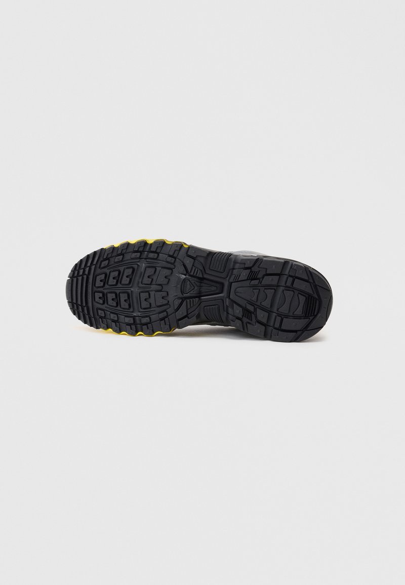 Semelle de chaussure de sport noire avec caoutchouc texturé, dotée de profondes rainures et d'accents jaunes. Conçue pour l'adhérence et la durabilité.