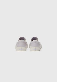 Sapatos slip-on de tela lilás claro com uma forma arredondada, solas de borracha creme e um detalhe de logotipo subtil na parte de trás.