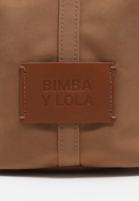Brązowa torba z płótna z wytłoczonym skórzanym znaczkiem "BIMBA Y LOLA." Posiada pionową szew i gładką powierzchnię z materiału.