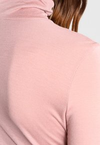 Rosa polokrage topp i mjukt, texturerat tyg. Har en vikbar krage och en figursydd silhuett som framhäver en slät look.