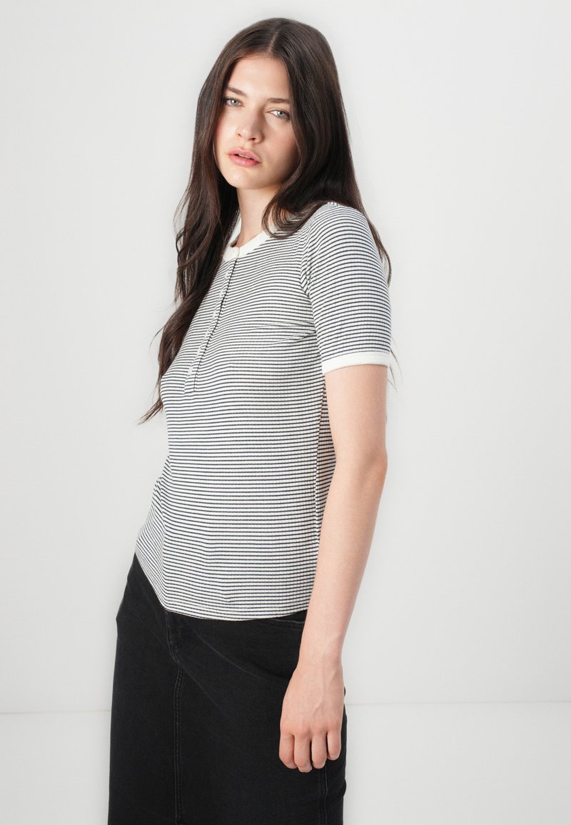 Pasiasta koszulka w czarno-białe paski, z krótkimi rękawami i okrągłym dekoltem. Posiada teksturowany materiał oraz biały kołnierzyk.