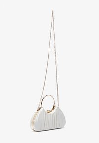 Sac à main plissé blanc avec une poignée en métal en forme d'anneau et une bandoulière en chaîne dorée, présentant une texture horizontale et une forme courbée et douce.