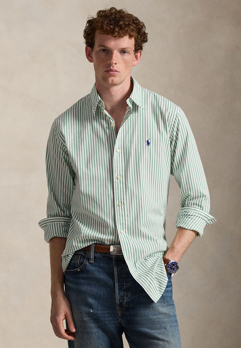 Green and white striped button-up shirt made of fabric with a soft texture. Features a small embroidered logo on the chest and rolled sleeves.