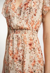 Robe à motifs floraux en tissu beige léger avec des accents texturés. Présente une taille smockée et des manches courtes.