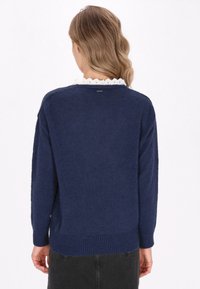 Granatowy sweter wykonany z fakturowanej dzianiny, z falbaniastym białym kołnierzem oraz luźnym krojem z ribbowanym hemem i mankietami.