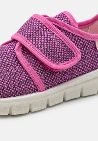 Sapato com padrão em tons de roxo e rosa, com uma faixa de Velcro, sola branca espessa, tecido texturizado e design de bico arredondado.