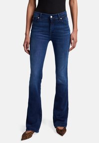 Jean flare bleu foncé en denim, avec une taille haute, des poches et une texture lisse, associés à des talons aiguilles en imprimé léopard.