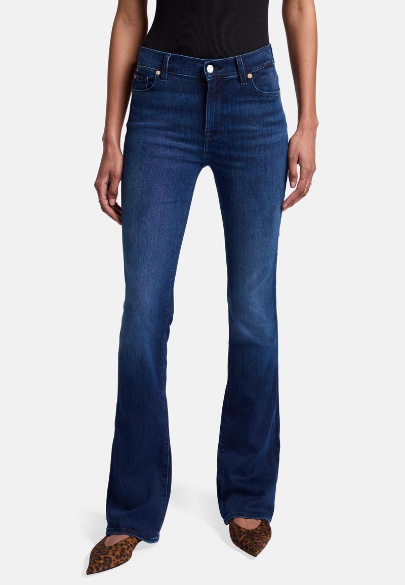 Jean flare bleu foncé en denim, avec une taille haute, des poches et une texture lisse, associés à des talons aiguilles en imprimé léopard.