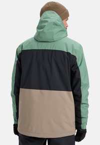 Multicolored jacket featuring a hood, made of smooth fabric. Colors include mint green, black, and beige, with a block design and front pockets.