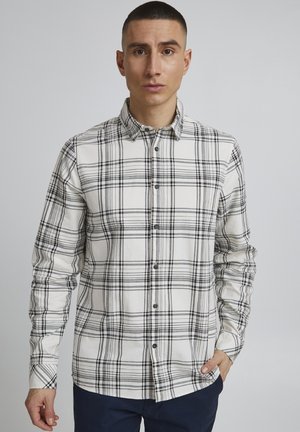 Camisa de cuadro en algodón blanco y negro con cuello abotonado, mangas largas y dobladillo recto. Presenta botones negros y un ajuste relajado.