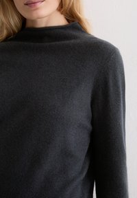 Dunkelgrauer, hochgeschlossener Pullover aus weichem Strickstoff, mit langen Ärmeln und glatter Textur. Keine sichtbaren Muster oder Akzente.