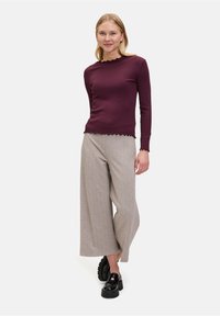 Haut à manches longues bourgogne avec des bords festonnés, associé à un pantalon large gris clair et des chaussures à plateforme noires. Texture lisse dans l'ensemble.
