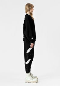 Sudadera negra de gran tamaño y pantalones jogger con patrones de plumas blancas, combinados con botas blancas gruesas, que muestran un ajuste relajado y un tejido suave.