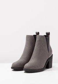 Szare ankle boots z sztucznego zamszu z elastycznymi bocznymi panelami i uchwytami. Posiadają teksturowany czarny blokowy obcas i zaokrąglony czubek.